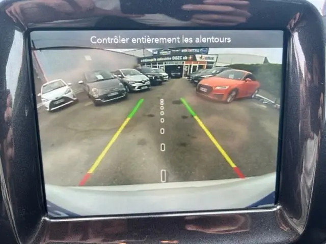 Vue arrière depuis la caméra de recul d'un Jeep Compass blanc hybride rechargeable, montrant un parking avec plusieurs voitures.