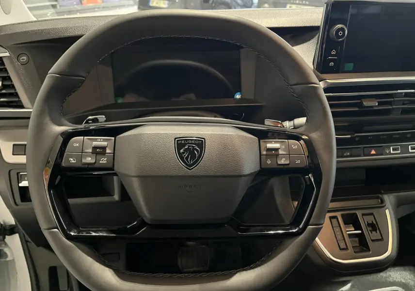 Vue rapprochée du volant en cuir noir du Peugeot Expert Fourgon 2024 avec commandes intégrées et tableau de bord moderne.