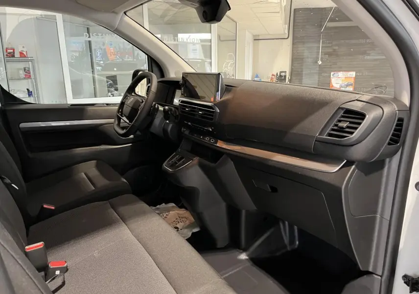 Intérieur côté conducteur du Peugeot Expert Fourgon blanc 2024, planche de bord noire avec écran tactile et sièges tissu bi-ton noir-gris.