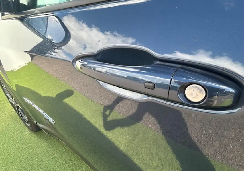 Poignée de porte côté gauche du Jeep Compass 2022 en peinture métallisée Blue Shade reflétant ciel et herbe.