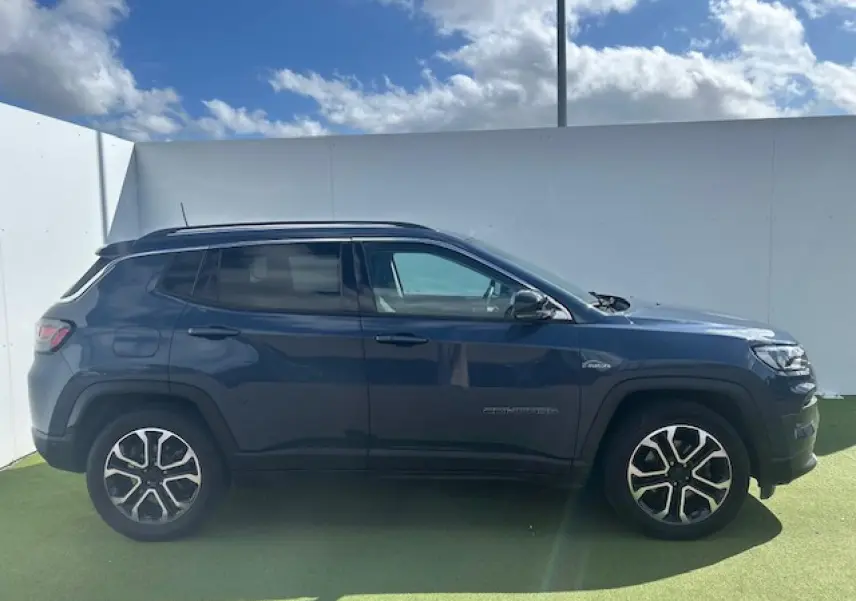 Jeep Compass 2022 bleu métallisé en profil côté gauche, avec jantes alliage et barres de toit visibles.