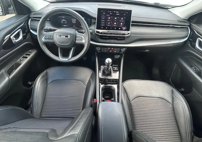 Vue intérieure avant du Jeep Compass 2022 avec tableau de bord noir, écran tactile et levier de vitesses manuel.