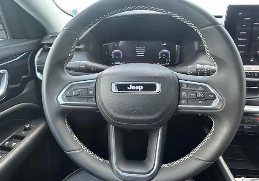 Vue rapprochée du volant noir avec surpiqûres blanches et tableau de bord numérique du Jeep Compass 2022.