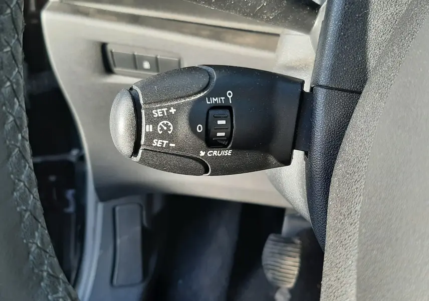 Gros plan sur la commande de régulateur de vitesse noire à gauche du volant d'une Citroën C3 noire de 2016.