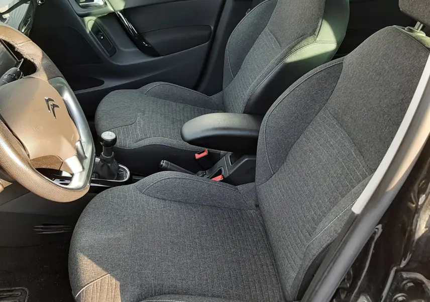 Intérieur de la Citroën C3 noire, vue côté gauche montrant les sièges en tissu gris et le volant avec levier de vitesse manuel.