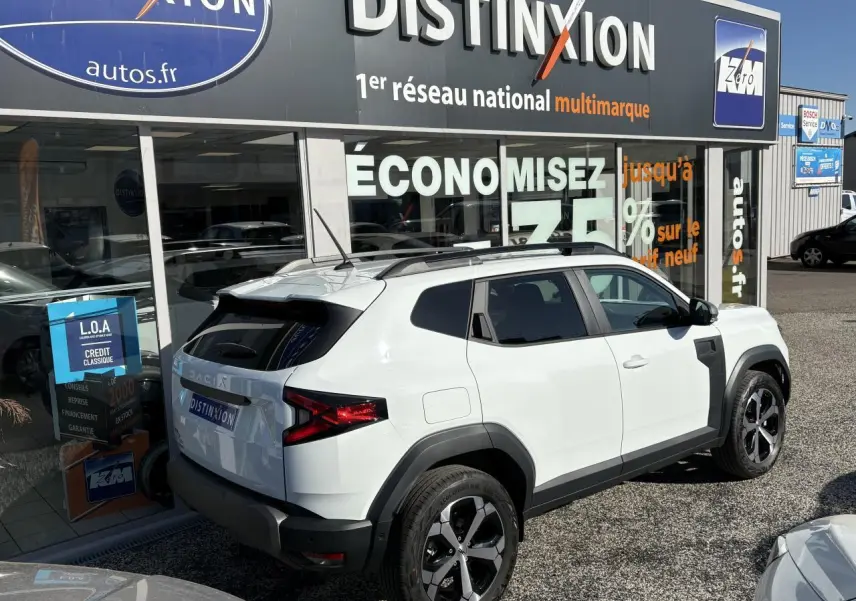 Vue 3/4 arrière droite du Dacia Duster blanc métallisé avec barres de toit noires et jantes alliage 18 pouces.