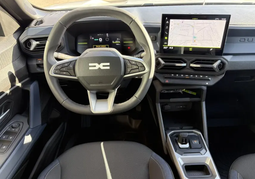 Vue intérieure frontale du tableau de bord du Dacia Duster 2024, avec volant multifonction, écran tactile et sellerie Denim noire.