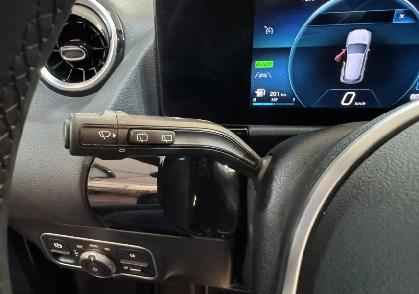 Gros plan sur la commande d’essuie-glace à gauche du volant cuir noir dans le tableau de bord numérique d’une Mercedes GLA 250 e gris foncé.