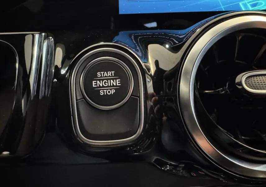 Gros plan sur le bouton start/stop moteur noir entouré de chrome dans l’habitacle du Mercedes GLA 250 e gris foncé.