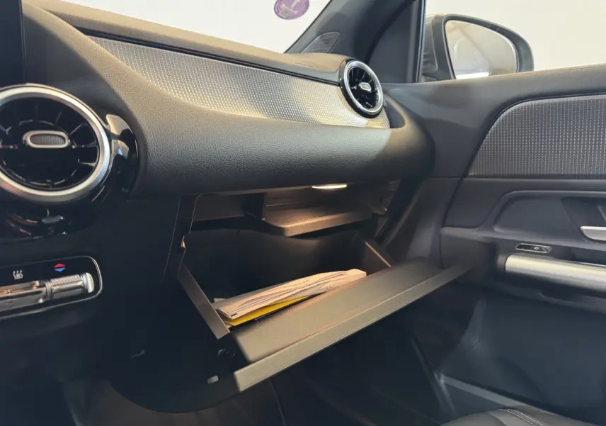 Intérieur côté passager du Mercedes GLA 250 e gris foncé 2023 avec boîte à gants ouverte et aérateurs ronds noirs.