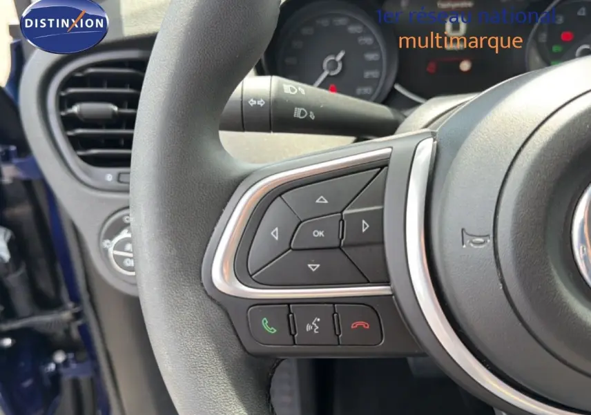 Gros plan sur le volant de la FIAT 500X bleu Venezia, montrant les commandes intégrées et la partie gauche du tableau de bord.