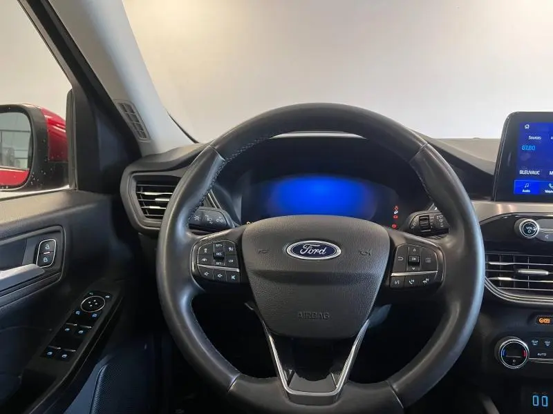 Vue intérieure centrée sur le volant cuir multifonction du Ford Kuga rouge avec tableau de bord et écran tactile visible