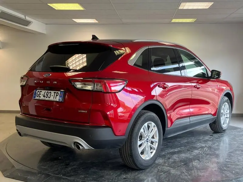 Vue 3/4 arrière droite d'un Ford Kuga 2022 hybride en rouge Premium Lucid avec toit panoramique et vitres arrière surteintées.