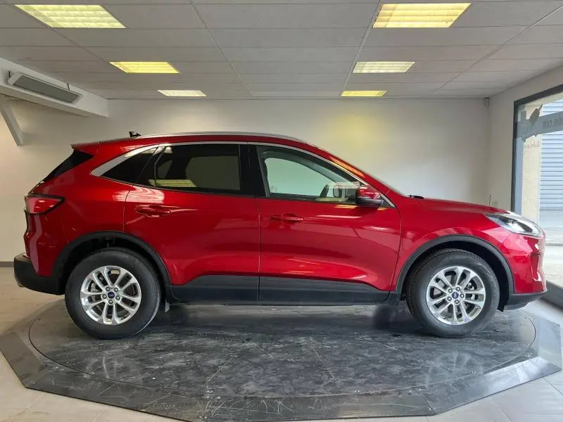 Profil droit d'un Ford Kuga 2022 hybride en rouge Premium Lucid avec vitres arrière surteintées en intérieur showroom.