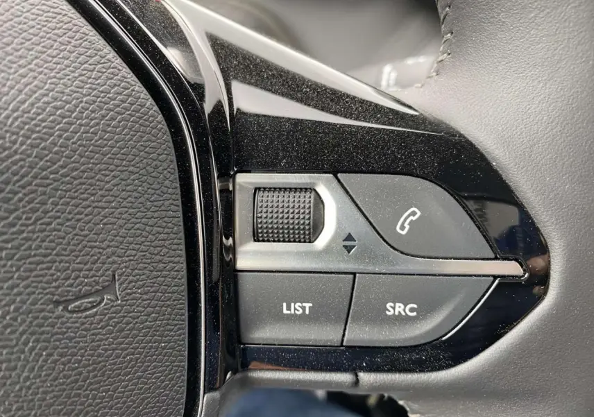 Gros plan sur les commandes du volant noir métallisé d'une Peugeot 208 2023, boutons list, SRC et appel téléphonique.