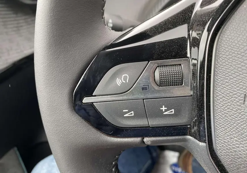 Gros plan sur les commandes audio et vocales au volant d'une Peugeot 208 noire métallisée de 2023.