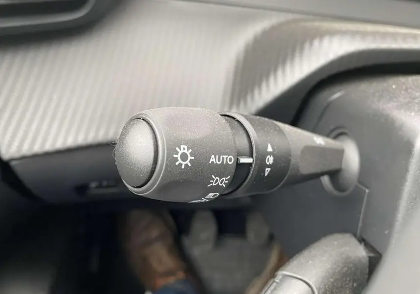 Gros plan sur la commande des feux avec réglage automatique dans l'habitacle d'une Peugeot 208 noire métallisée 2023.