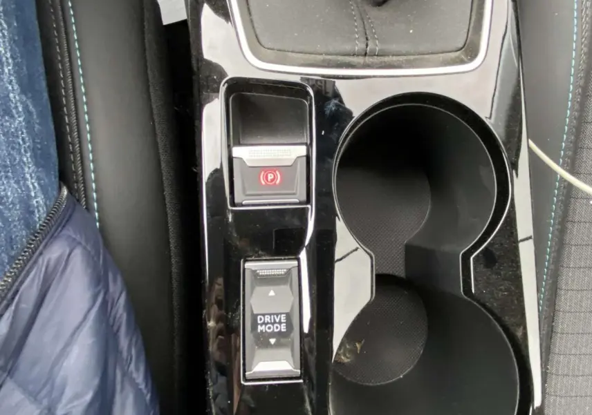 Gros plan sur la console centrale noire brillante d’une Peugeot 208 2023 avec frein à main électrique et bouton Drive Mode.