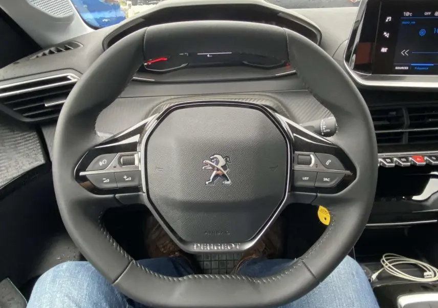 Vue intérieure centrée sur le volant cuir du Peugeot 208 2023 avec tableau de bord numérique et écran tactile.