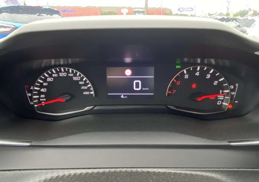 Vue rapprochée du tableau de bord numérique de la Peugeot 208 noire, affichant 0 km/h et 4 km au compteur.