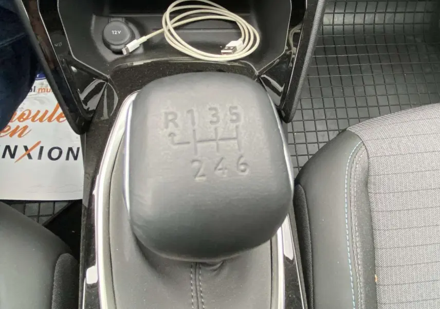 Gros plan sur le levier de vitesse manuel de la Peugeot 208 2023, intérieur noir avec surpiqûres bleues et câble USB.