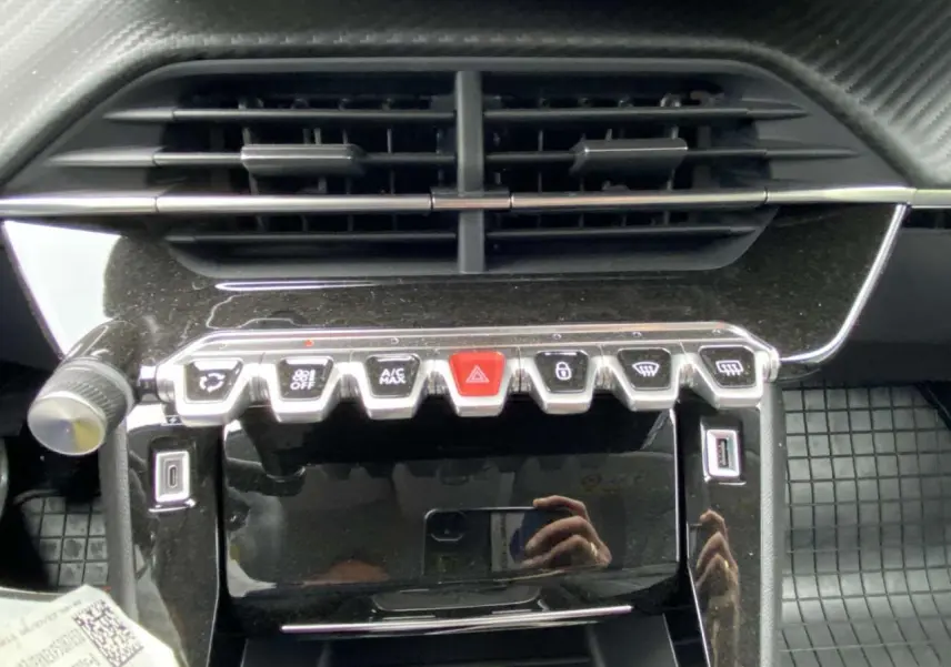 Vue rapprochée de la console centrale noire brillante de la Peugeot 208 avec boutons de commande et prises USB visibles.