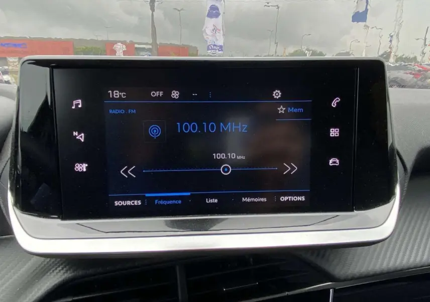 Écran tactile central de la Peugeot 208 2023 affichant la radio FM sur fond noir et détails lumineux blancs et bleus.