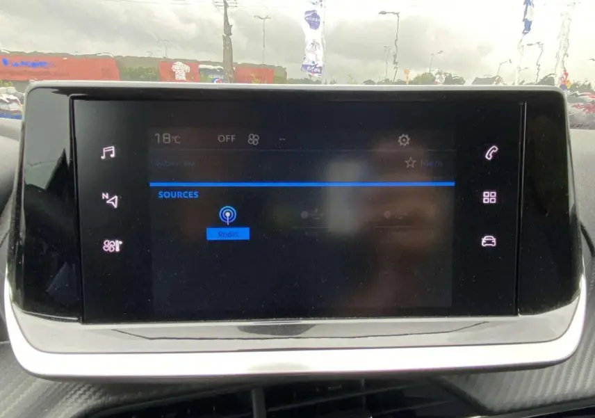 Écran tactile central de la Peugeot 208 2023 affichant les sources audio avec interface moderne et icônes lumineuses.