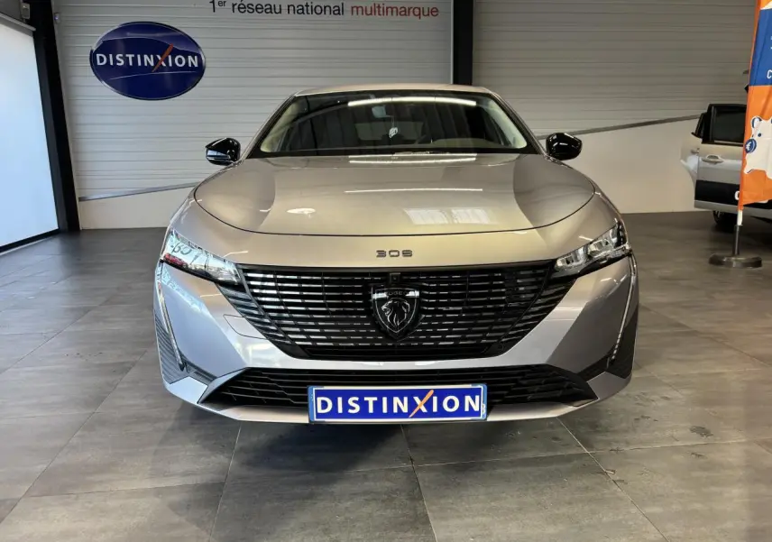 Vue frontale d'une Peugeot 308 SW gris clair métallisé avec calandre noire et logo lion central, en showroom.