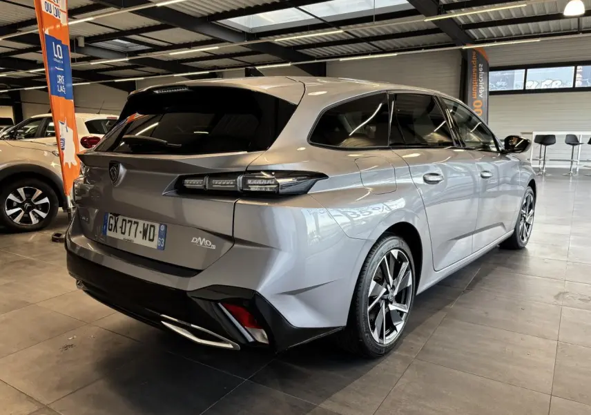 Vue 3/4 arrière droite d’un Peugeot 308 SW gris clair métallisé avec jantes alliage et feux LED distinctifs en intérieur showroom.