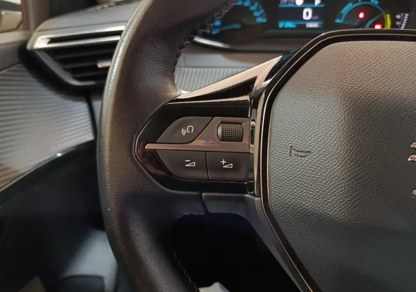 Gros plan sur le volant noir de la Peugeot 208 électrique 2020, avec commandes intégrées et tableau de bord lumineux en arrière-plan.