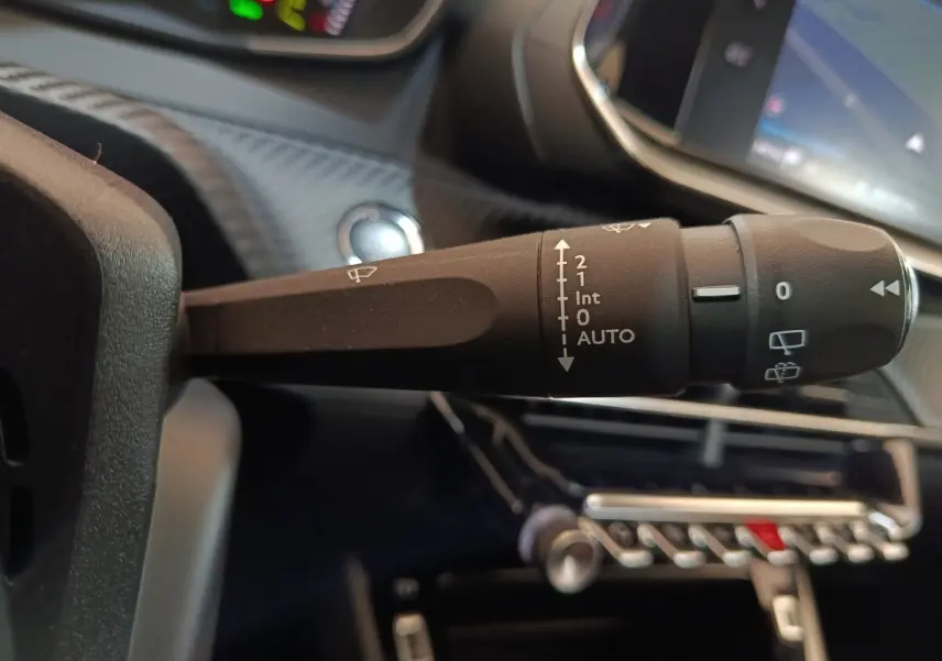 Gros plan sur la commande des essuie-glaces dans l’habitacle noir d’une Peugeot 208 électrique blanche.