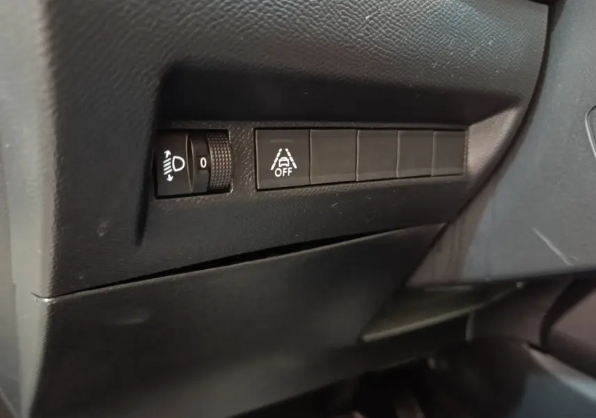 Détail des commandes d’éclairage et d’aide à la conduite sur tableau de bord noir du Peugeot 208 électrique.