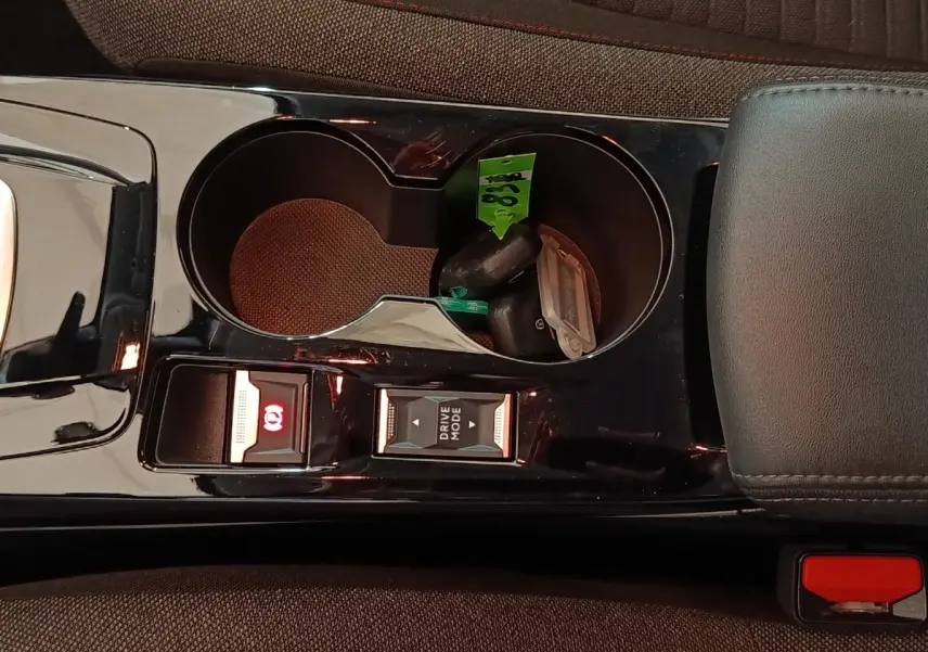 Gros plan sur la console centrale noire brillante de la Peugeot 208 électrique avec boutons frein à main et mode de conduite.