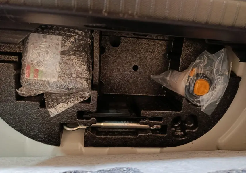 Vue du compartiment sous la banquette arrière d'une Peugeot 208 blanche, montrant le rangement d'outils et accessoires.