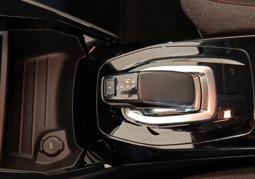 Gros plan sur la commande de boîte automatique noire au centre de la console d’une Peugeot 208 électrique blanche.