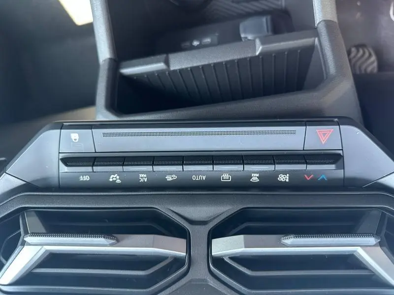 Vue rapprochée du tableau de bord du Dacia Duster blanc 2025, montrant les commandes climatisation et les aérateurs centraux.