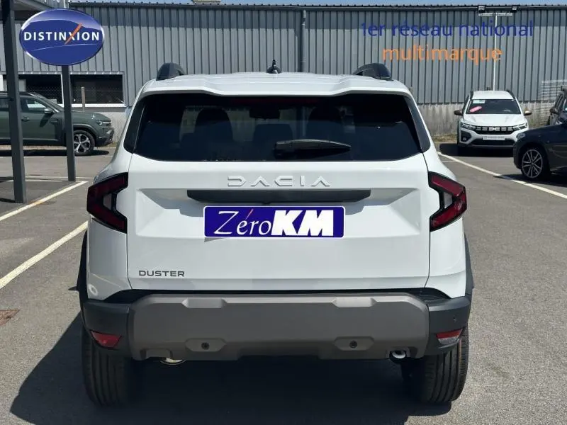 Vue arrière d'un Dacia Duster blanc Glacier 2025 avec lunette arrière surteintée et barres de toit noires.