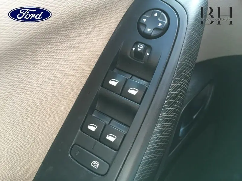 Panneau de commandes des vitres électriques côté conducteur avec boutons noirs sur garniture beige et poignée à motif gris.