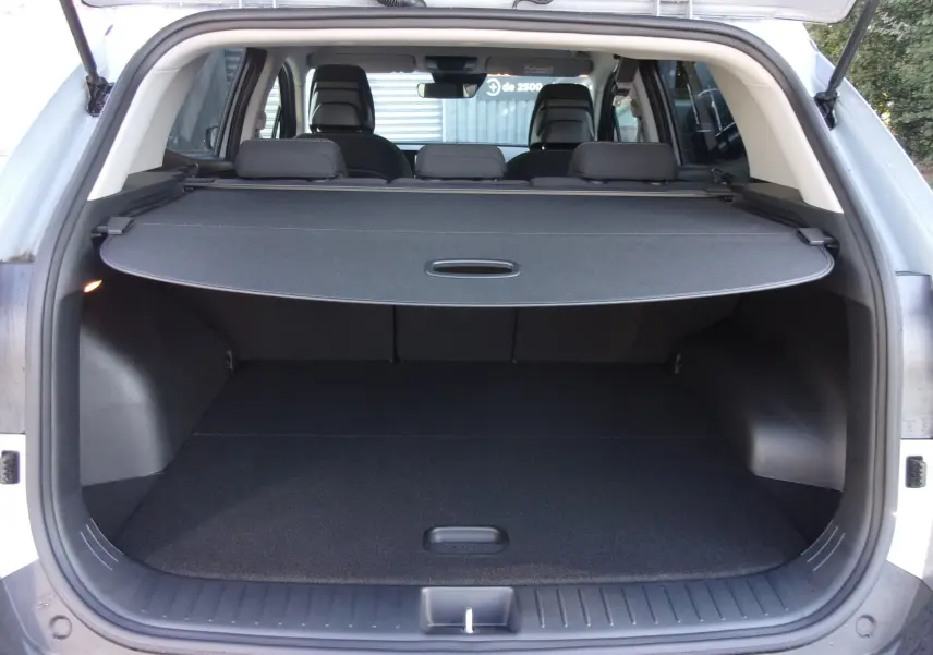 Coffre ouvert du KIA SPORTAGE gris perle vu de l'arrière, avec cache-bagages déployé et sièges arrière visibles.