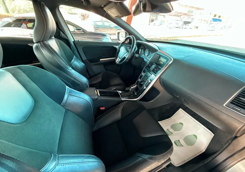 Vue intérieure côté conducteur du Volvo XC60 gris 2016, montrant sièges cuir noirs et tableau de bord moderne.