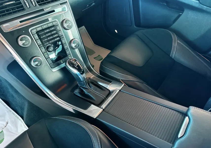 Vue intérieure centrée sur la console centrale et le levier de vitesse automatique du Volvo XC60 gris, sièges noirs en cuir et alcantara.