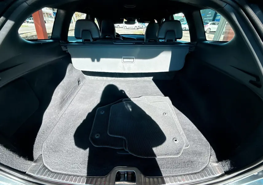 Vue du coffre ouvert d'un Volvo XC60 gris 2016, montrant l'espace de chargement avec tapis de sol et cache-bagages.