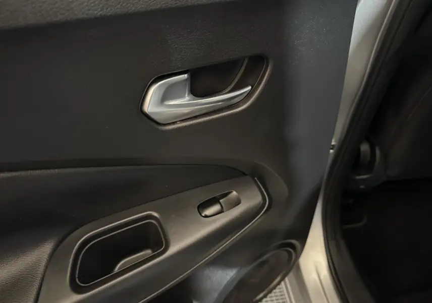 Poignée intérieure et commande de vitre sur la porte arrière droite d'un Nissan Juke gris clair, vue rapprochée.