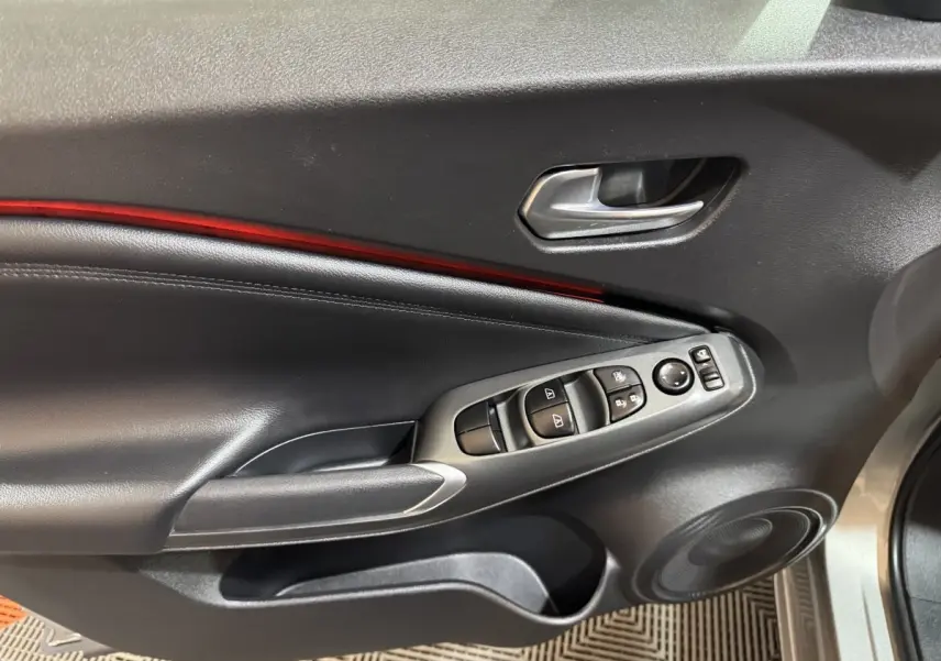 Vue intérieure côté gauche de la porte avant gris clair du Nissan Juke avec commandes vitres et bandeau lumineux rouge.