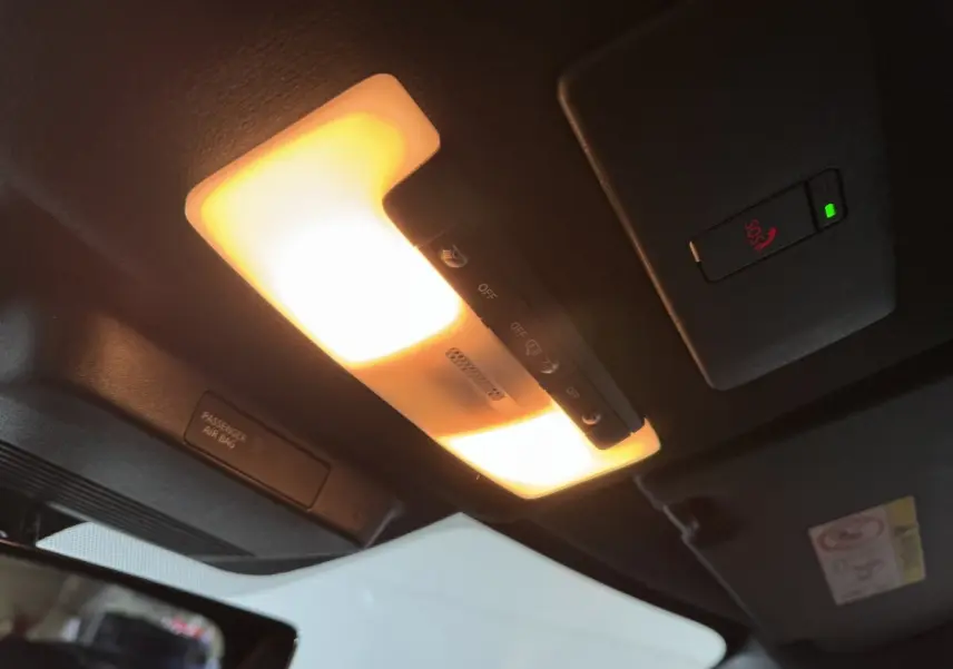Vue intérieure du plafond du Nissan Juke gris clair 2025, avec éclairage intérieur et bouton SOS allumé.