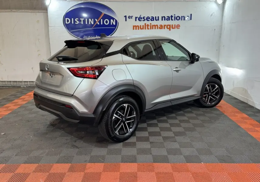 Vue 3/4 arrière droite d'un Nissan Juke gris clair 2025 avec jantes noires et vitres teintées en intérieur showroom.