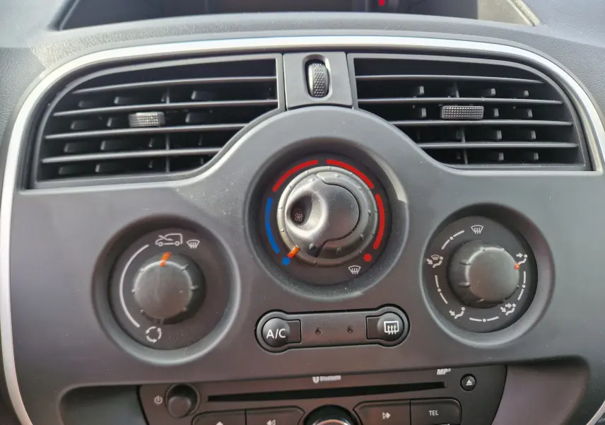 Vue rapprochée du tableau de bord du Renault Kangoo blanc 2021, montrant les commandes de climatisation et la ventilation centrale.