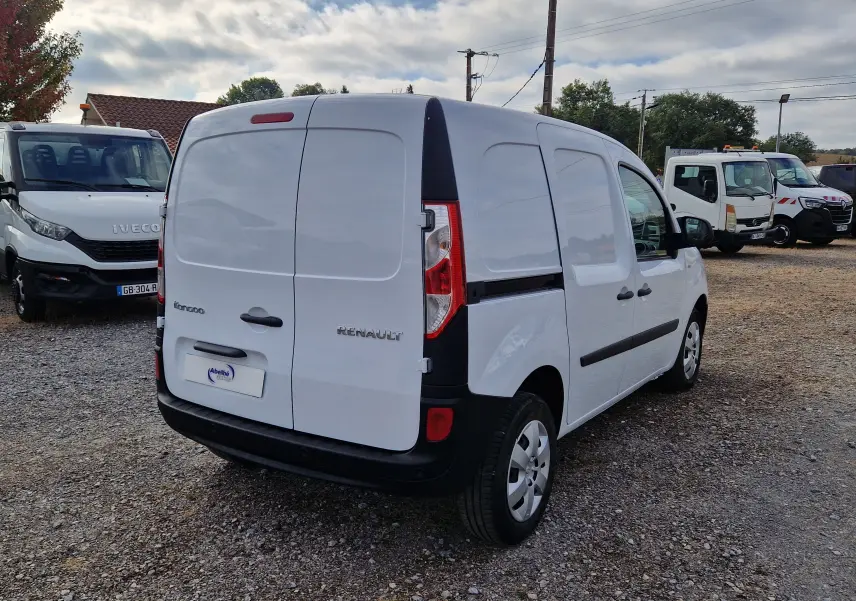 Vue 3/4 arrière droite d’un Renault Kangoo blanc utilitaire avec portes arrière battantes sur un parking gravelé.