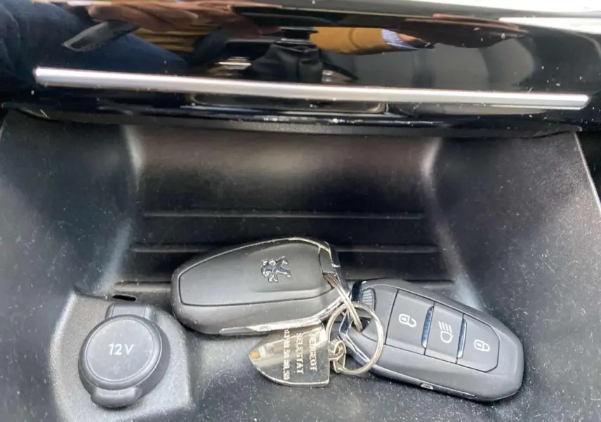 Gros plan sur les deux télécommandes noires Peugeot posées près de la prise 12V dans la console avant du véhicule.